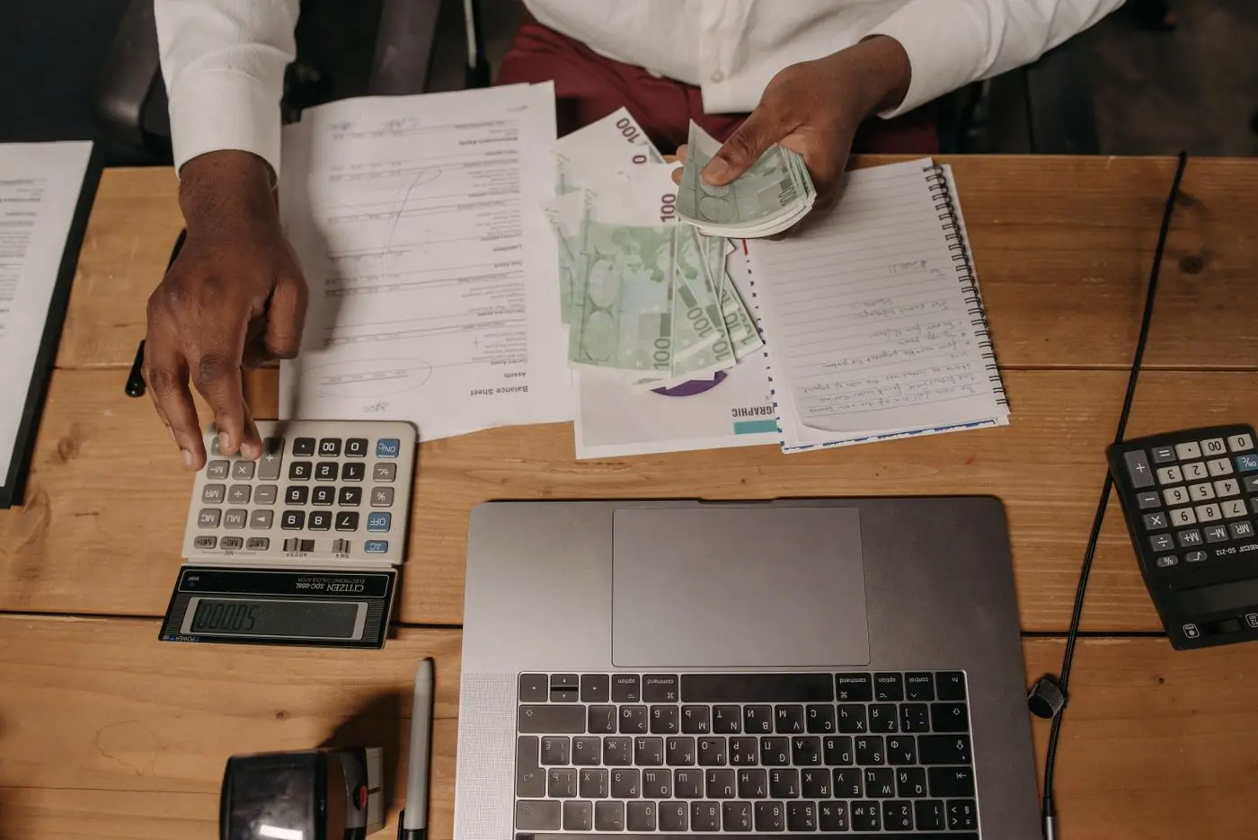 Financial records, cash and a laptop on an office desk